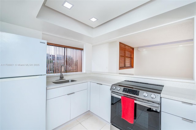 kitchen featuring sink, light tile patterned floors, white fridge, stainless steel range with electric stovetop, and white cabinets