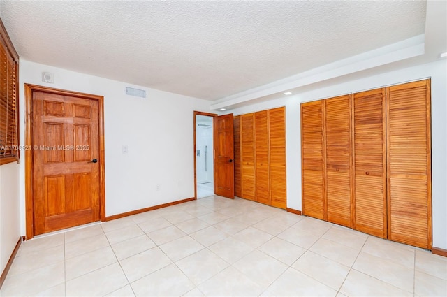 unfurnished bedroom featuring a textured ceiling, multiple closets, and light tile patterned flooring