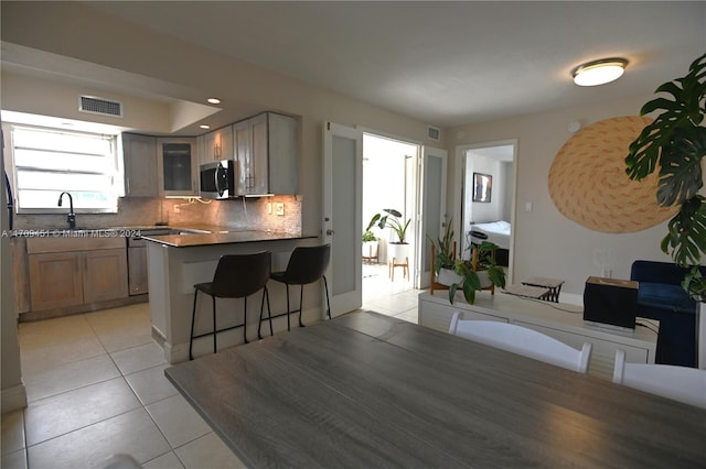 kitchen featuring sink, a kitchen breakfast bar, kitchen peninsula, decorative backsplash, and light tile patterned floors