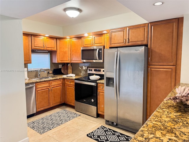 kitchen featuring light stone counters, light tile patterned flooring, brown cabinetry, stainless steel appliances, and a sink