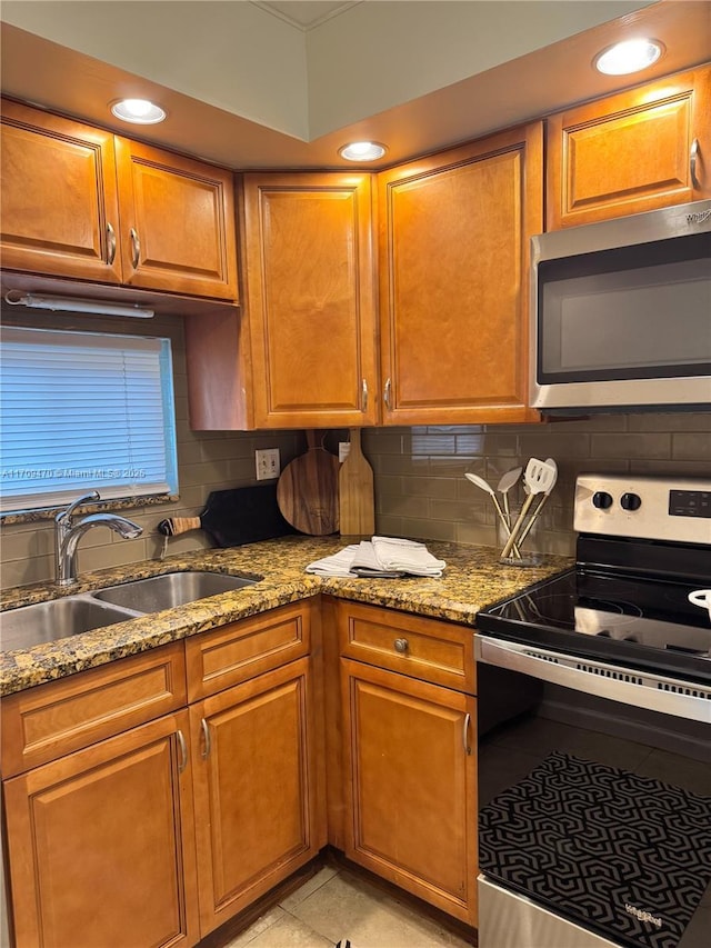 kitchen with light stone counters, a sink, stainless steel appliances, brown cabinets, and backsplash