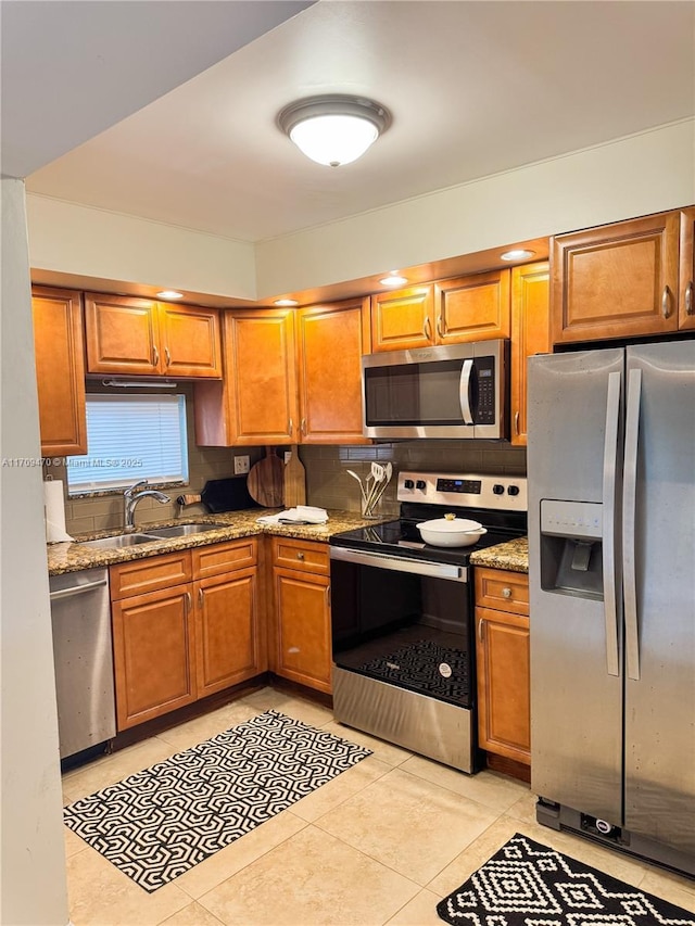 kitchen featuring a sink, stainless steel appliances, brown cabinets, and light stone counters