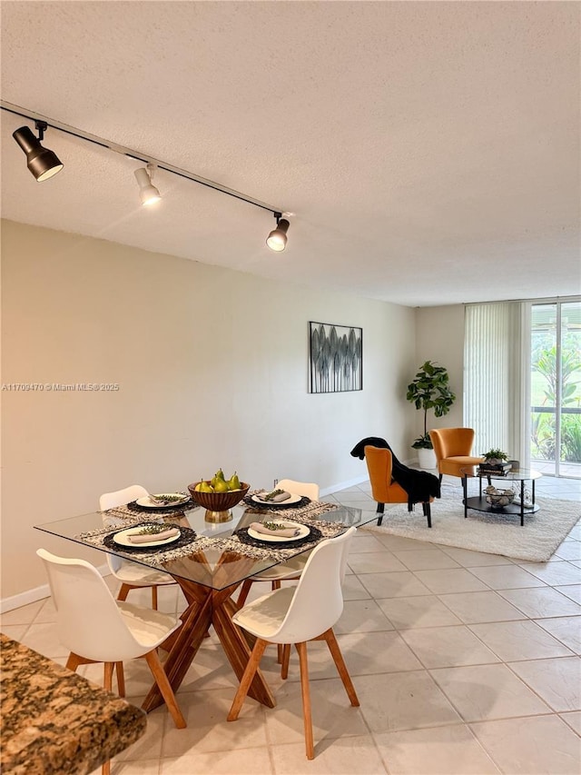 dining room featuring baseboards, a textured ceiling, light tile patterned flooring, and rail lighting