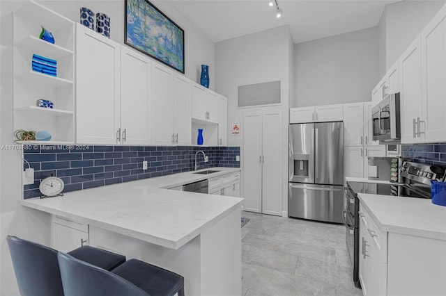 kitchen featuring a kitchen bar, sink, light stone counters, white cabinetry, and stainless steel appliances