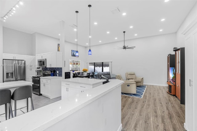 kitchen featuring light stone countertops, ceiling fan, stainless steel appliances, a high ceiling, and white cabinets