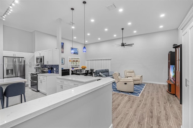 kitchen with light stone countertops, appliances with stainless steel finishes, a towering ceiling, light hardwood / wood-style flooring, and white cabinetry