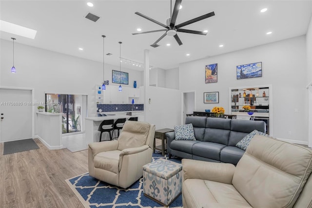 living room featuring a skylight, a towering ceiling, light hardwood / wood-style floors, and ceiling fan