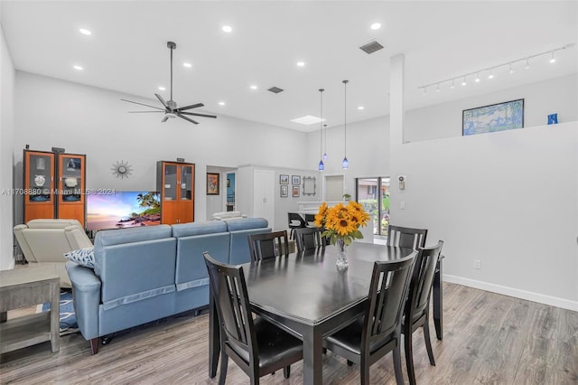 dining space with ceiling fan, track lighting, wood-type flooring, and a high ceiling