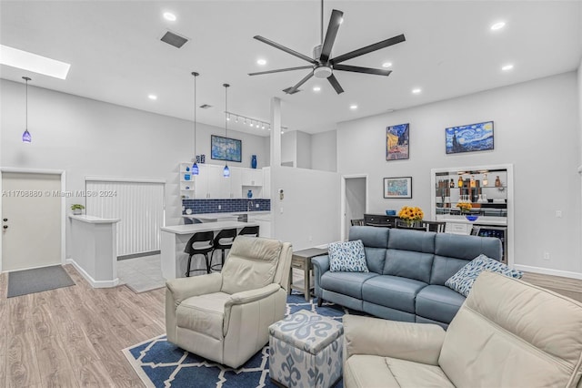 living room featuring ceiling fan, a skylight, a towering ceiling, and light hardwood / wood-style flooring