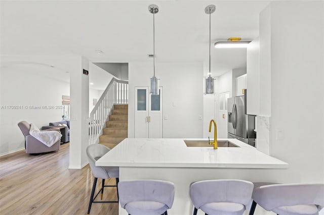 kitchen with pendant lighting, sink, stainless steel fridge, light wood-type flooring, and kitchen peninsula