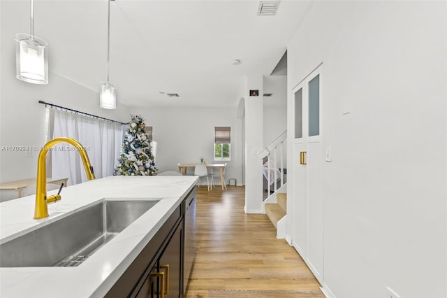 kitchen featuring stainless steel dishwasher, light stone counters, sink, decorative light fixtures, and light hardwood / wood-style floors