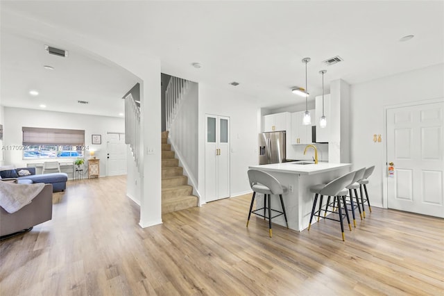 kitchen with kitchen peninsula, a breakfast bar, pendant lighting, white cabinets, and stainless steel fridge with ice dispenser