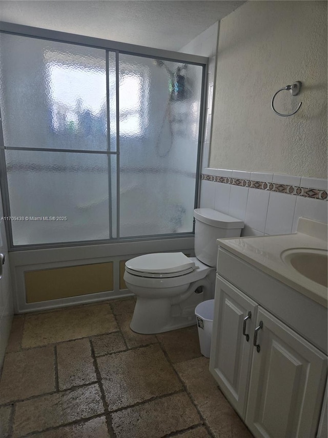 full bathroom featuring enclosed tub / shower combo, vanity, toilet, and tile walls