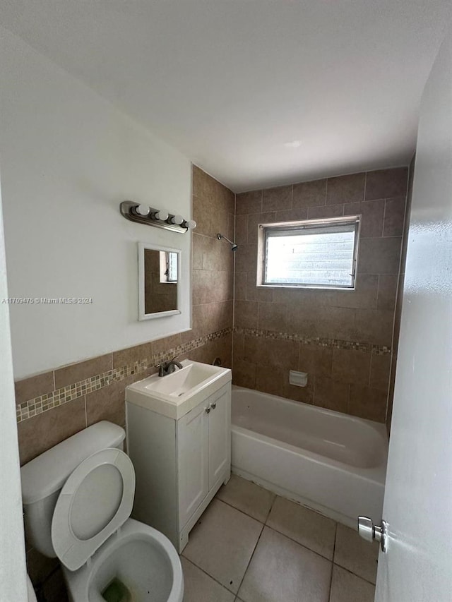 full bathroom featuring tiled shower / bath combo, tile patterned floors, toilet, vanity, and tile walls