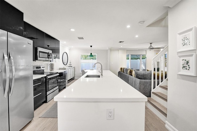 kitchen with a center island with sink, sink, hanging light fixtures, light hardwood / wood-style flooring, and stainless steel appliances