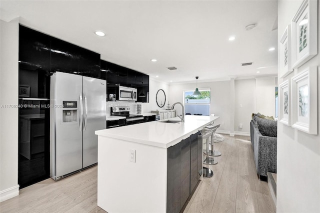 kitchen featuring sink, stainless steel appliances, an island with sink, pendant lighting, and light wood-type flooring