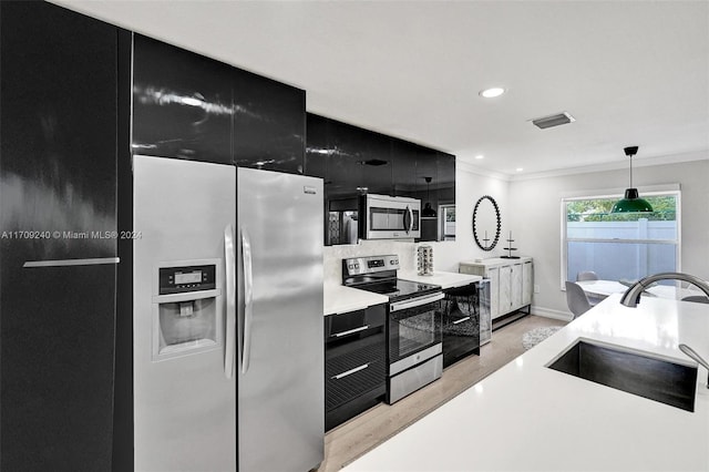 kitchen featuring pendant lighting, sink, ornamental molding, appliances with stainless steel finishes, and light hardwood / wood-style floors