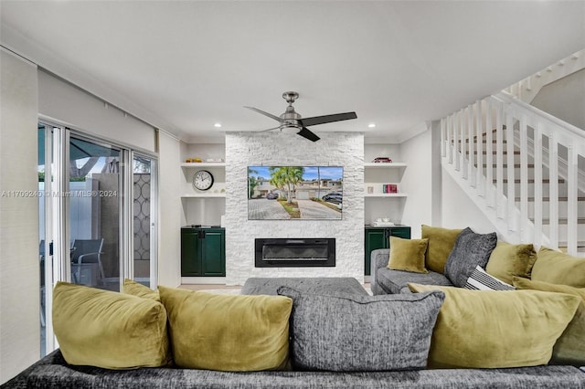 living room with built in features, a stone fireplace, ceiling fan, and ornamental molding