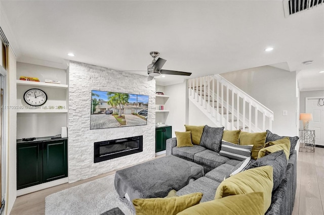 living room featuring ceiling fan, a stone fireplace, built in features, and light hardwood / wood-style flooring