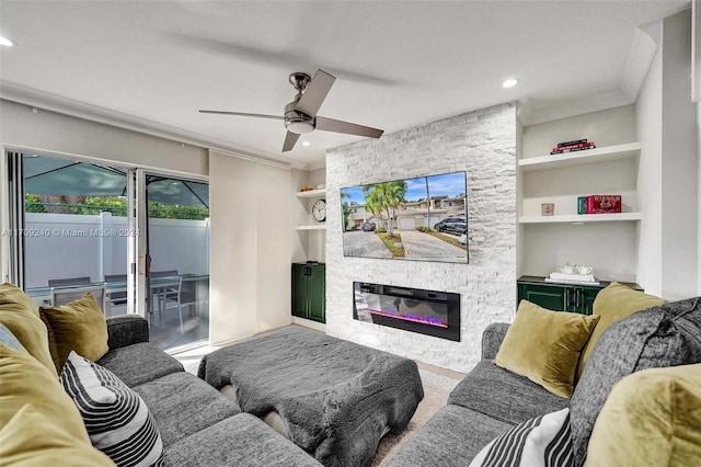 living room with built in shelves, a stone fireplace, ceiling fan, and ornamental molding