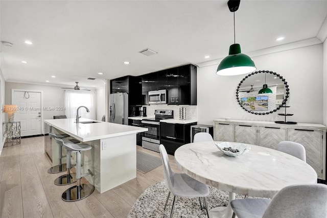 kitchen with pendant lighting, light hardwood / wood-style flooring, decorative backsplash, an island with sink, and stainless steel appliances