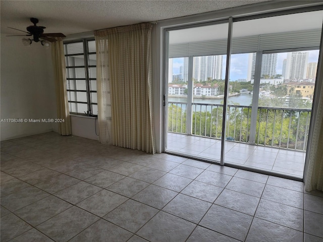 spare room featuring tile patterned floors, a water view, plenty of natural light, and ceiling fan