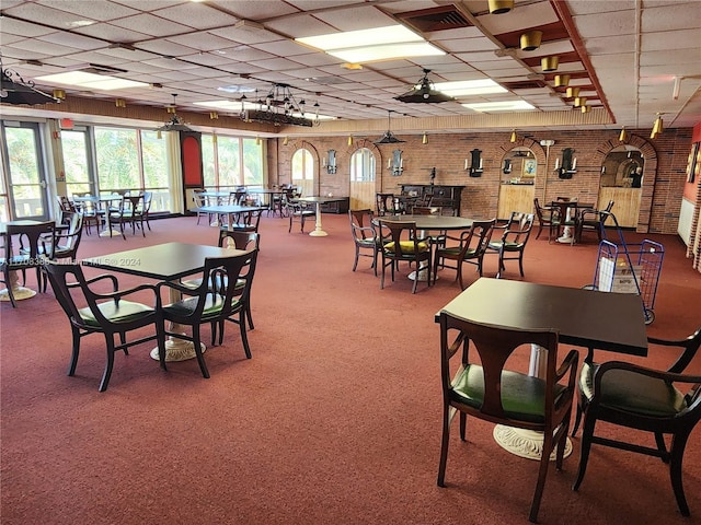 carpeted dining area with a drop ceiling and brick wall