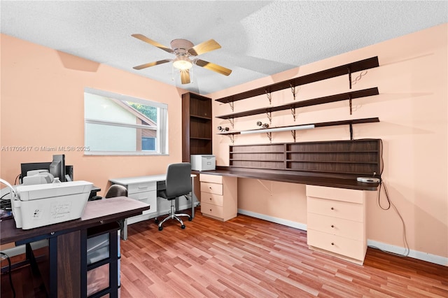 office space with ceiling fan, light hardwood / wood-style floors, built in desk, and a textured ceiling