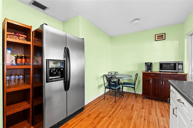 kitchen with light wood-type flooring, stainless steel refrigerator with ice dispenser, a textured ceiling, and white cabinetry