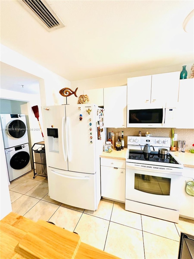 kitchen with stacked washer and dryer, white appliances, backsplash, white cabinets, and light tile patterned flooring