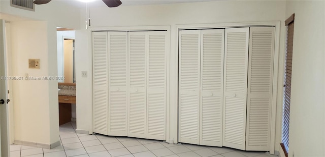 unfurnished bedroom featuring ceiling fan, light tile patterned floors, and multiple closets