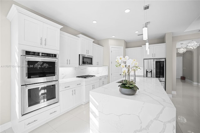 kitchen with a center island with sink, light stone countertops, decorative light fixtures, white cabinetry, and stainless steel appliances