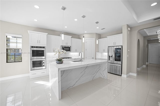 kitchen featuring white cabinetry, sink, stainless steel appliances, decorative light fixtures, and a center island with sink