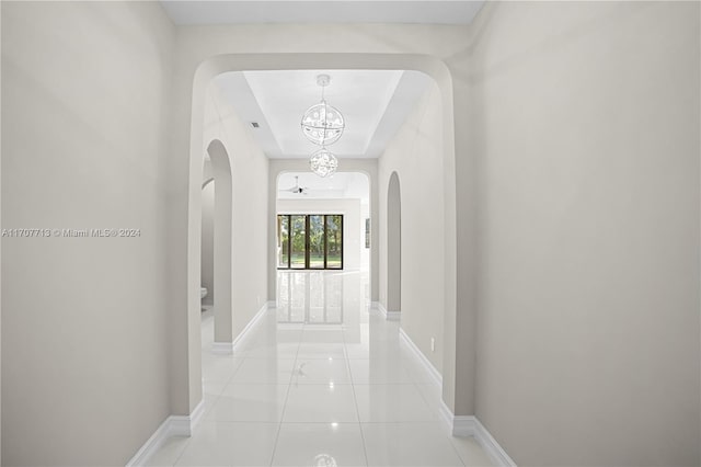 hall with a chandelier, light tile patterned floors, and a raised ceiling