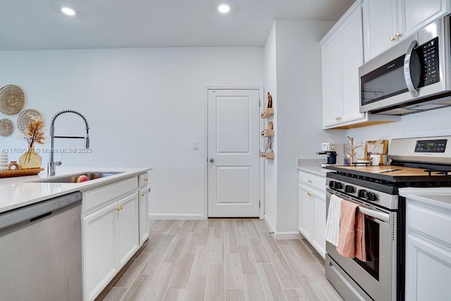 kitchen featuring appliances with stainless steel finishes, light wood-type flooring, white cabinetry, and sink