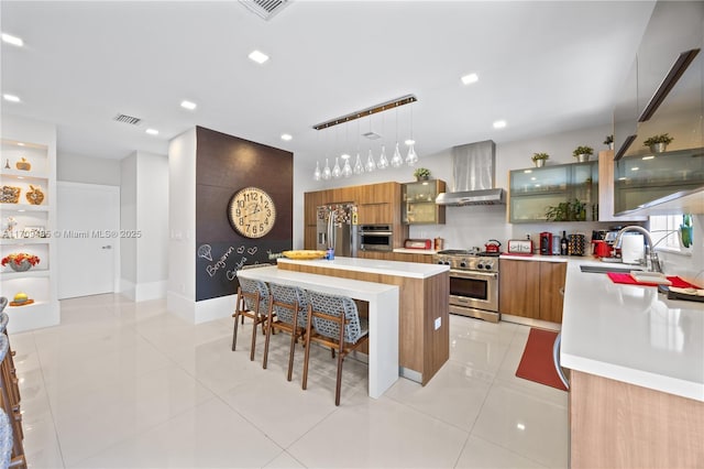 kitchen featuring a center island, wall chimney exhaust hood, stainless steel appliances, sink, and hanging light fixtures