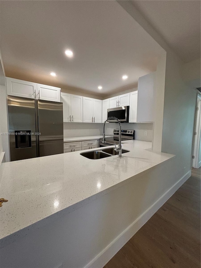 kitchen with white cabinets, dark hardwood / wood-style flooring, light stone counters, kitchen peninsula, and stainless steel appliances