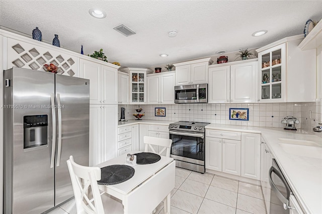 kitchen with light tile patterned floors, backsplash, stainless steel appliances, and white cabinetry