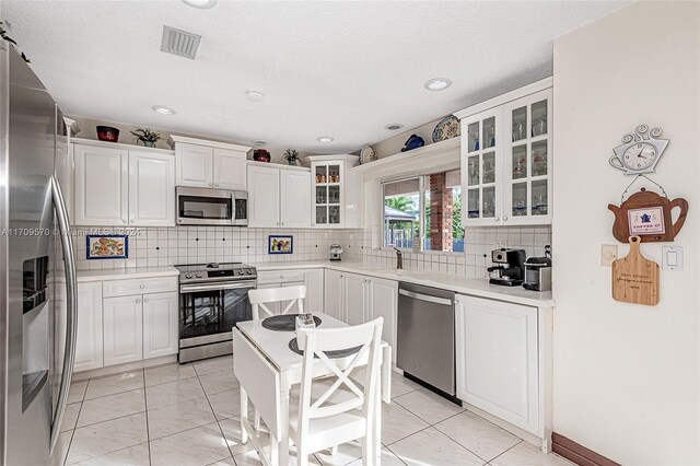 kitchen with white cabinets, decorative backsplash, light tile patterned floors, and stainless steel appliances