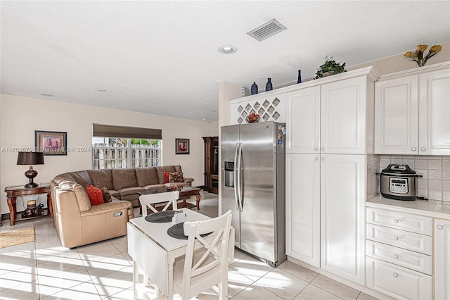 kitchen featuring stainless steel refrigerator with ice dispenser, backsplash, a textured ceiling, light tile patterned floors, and white cabinets