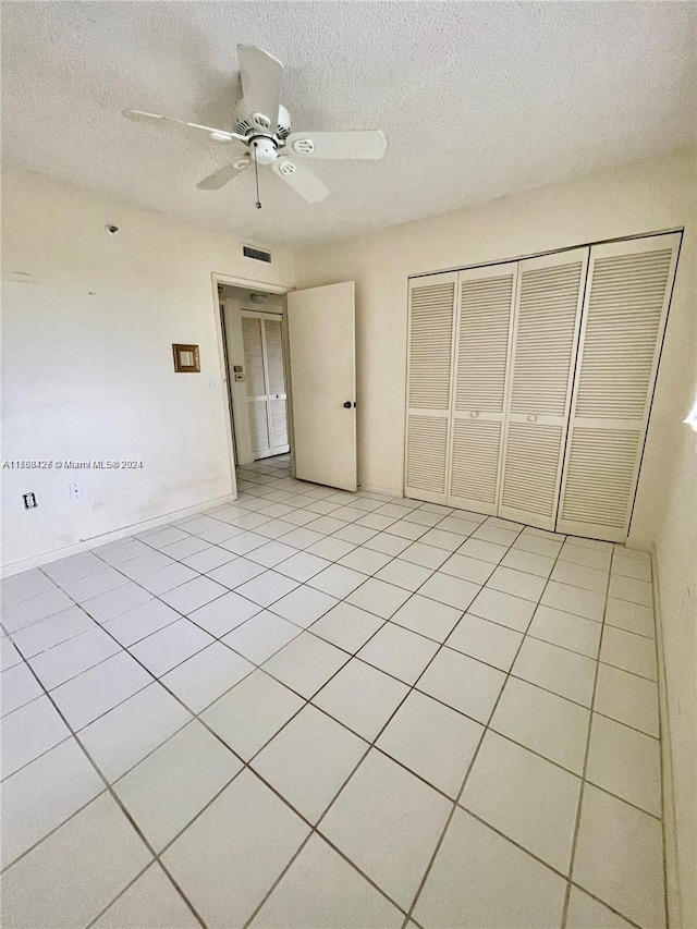 unfurnished bedroom with ceiling fan, a closet, light tile patterned floors, and a textured ceiling