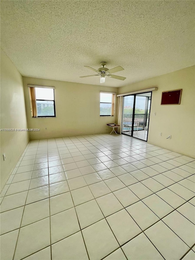 tiled empty room with ceiling fan and a textured ceiling