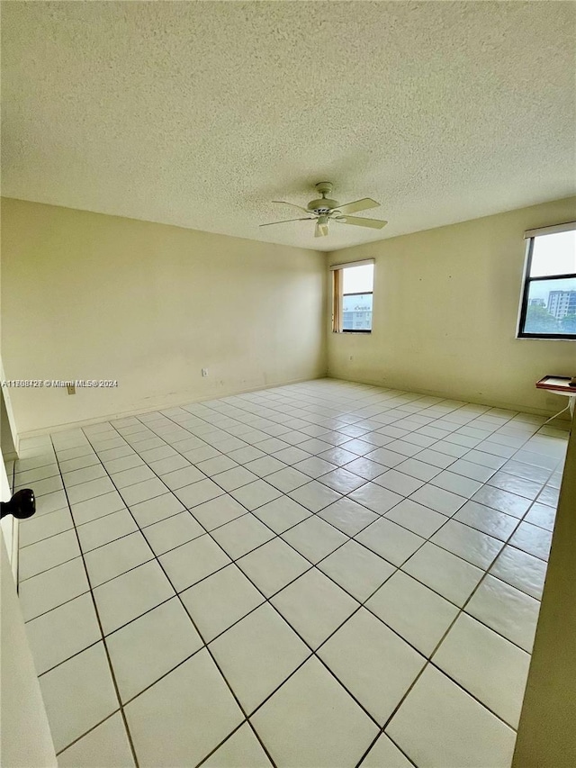 tiled spare room with a wealth of natural light, ceiling fan, and a textured ceiling