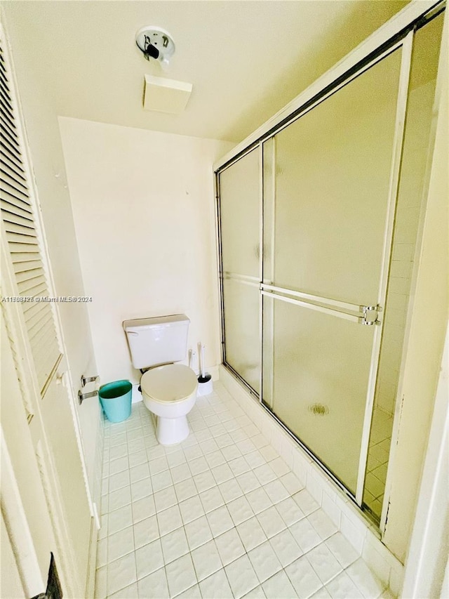 bathroom featuring tile patterned flooring, toilet, and a shower with door