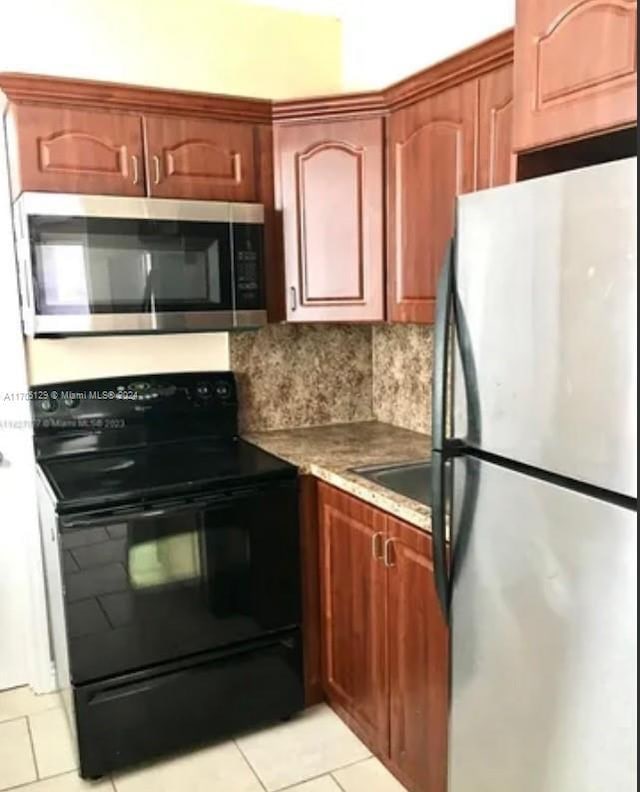 kitchen with decorative backsplash, light tile patterned flooring, light stone counters, and appliances with stainless steel finishes