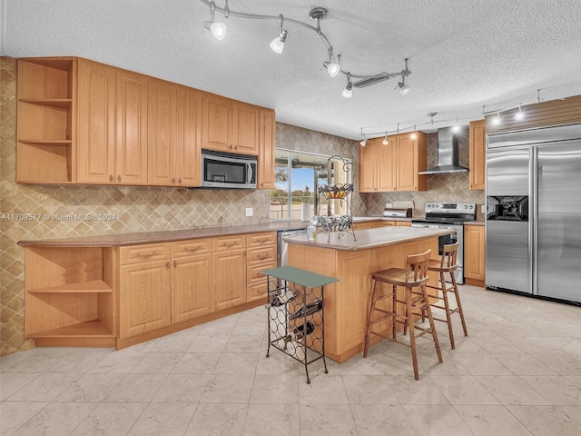 kitchen with wall chimney exhaust hood, a textured ceiling, a kitchen island, a kitchen bar, and stainless steel appliances