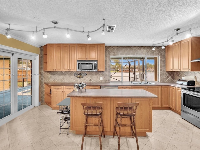 kitchen with appliances with stainless steel finishes, a kitchen breakfast bar, a textured ceiling, sink, and a center island