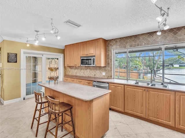 kitchen with ornamental molding, a textured ceiling, stainless steel appliances, sink, and a kitchen island