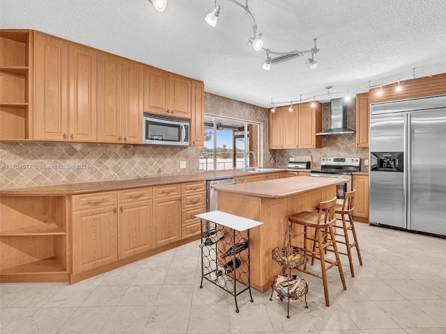 kitchen featuring a textured ceiling, stainless steel appliances, wall chimney range hood, a center island, and a breakfast bar area