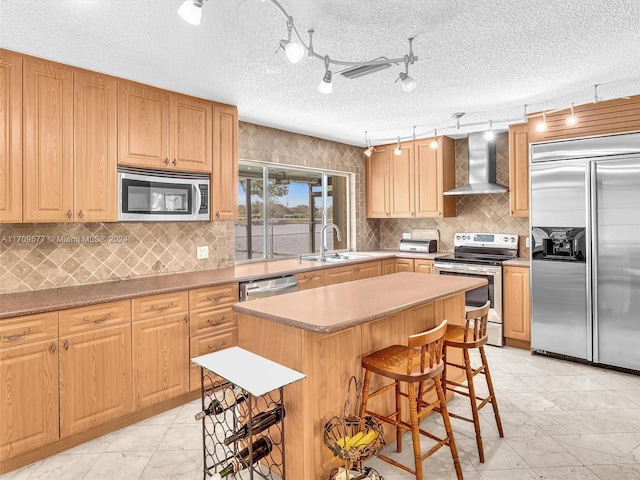 kitchen with wall chimney exhaust hood, a breakfast bar, a textured ceiling, stainless steel appliances, and a kitchen island